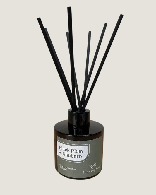 The Cosy Soul Reed diffuser with black reeds and a brown bottle labelled 'Black Plum & Rhubarb' on a light grey background