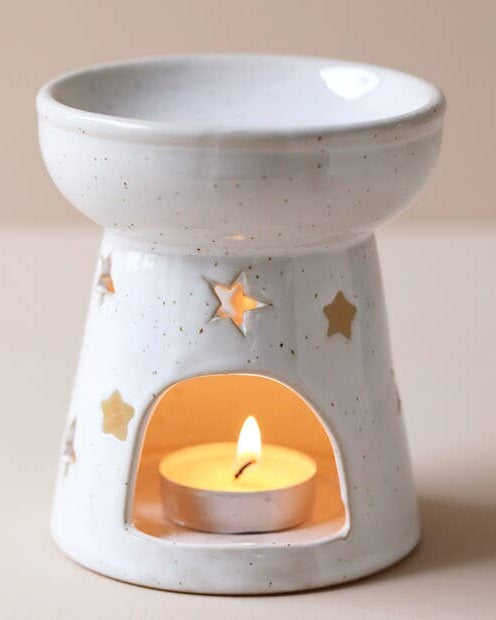 Ceramic oil burner with a lit candle inside on a beige background