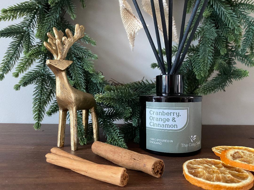 Cinnamon, Orange and Cranberry diffuser with cinnamon sticks, dried oranges, and a gold deer figurine on a wooden surface.
