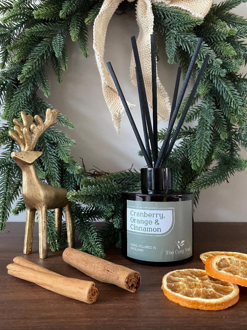 The Cosy Soul Diffuser with cinnamon sticks and dried oranges on a table with greenery in the background