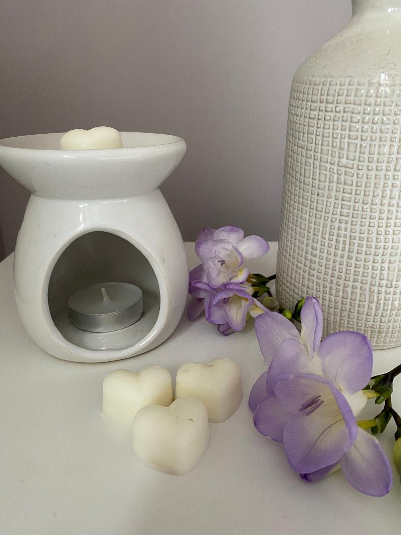 Fresh linen wax melts, a white wax melt burner, and purple freesias on a white surface.