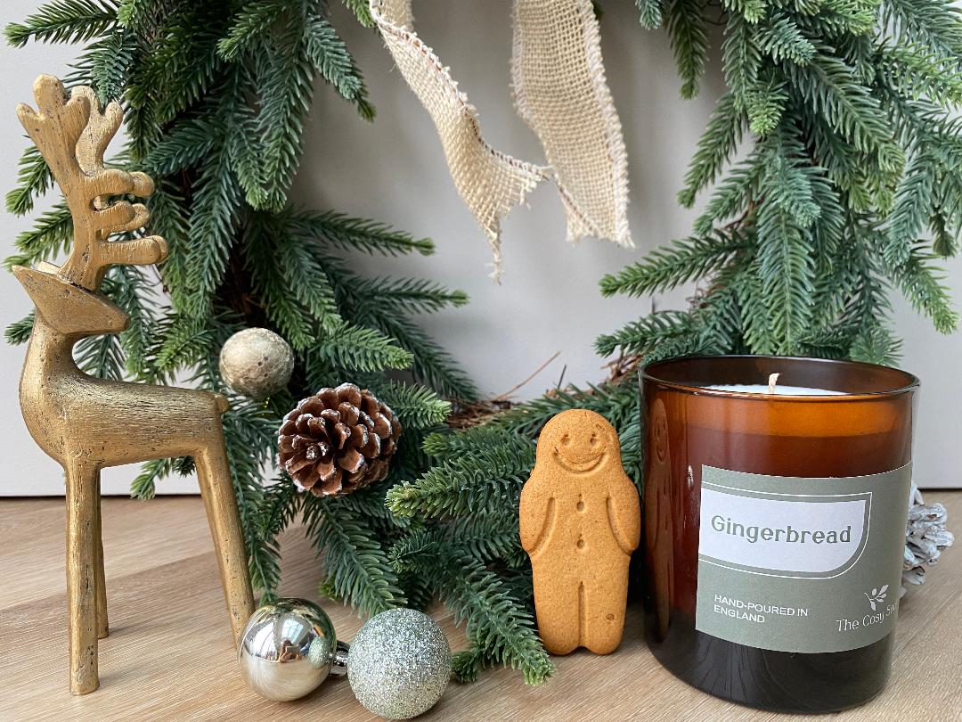 The Cosy Soul Gingerbread candle with decorative reindeer and Christmas tree on a wooden surface