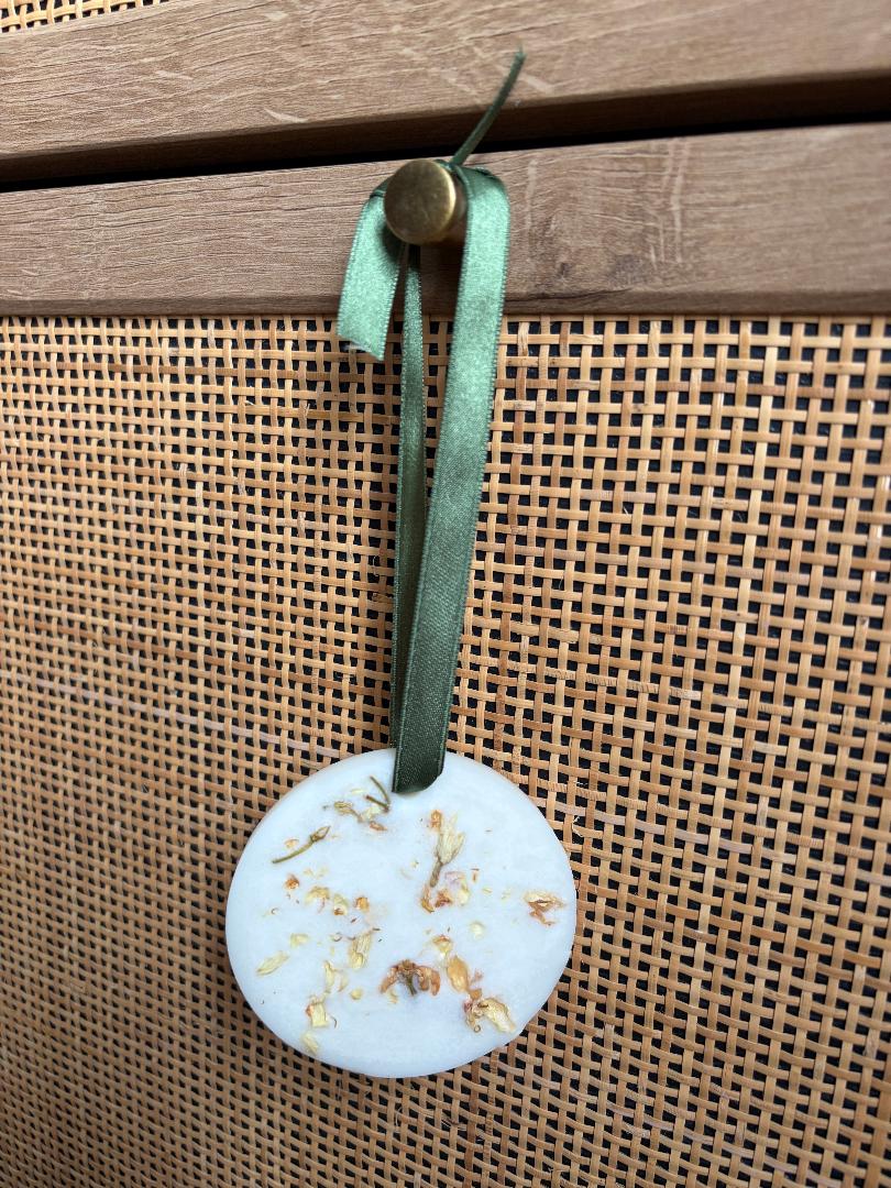Round hanging wax melt with a green ribbon on a textured surface
