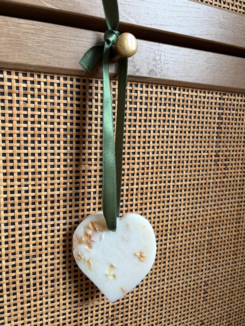 Heart-shaped wax melt hanging with a green ribbon on a woven surface