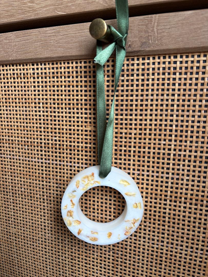 Hanging wax melt wreath with gold accents on a green ribbon, hanging on a wooden surface