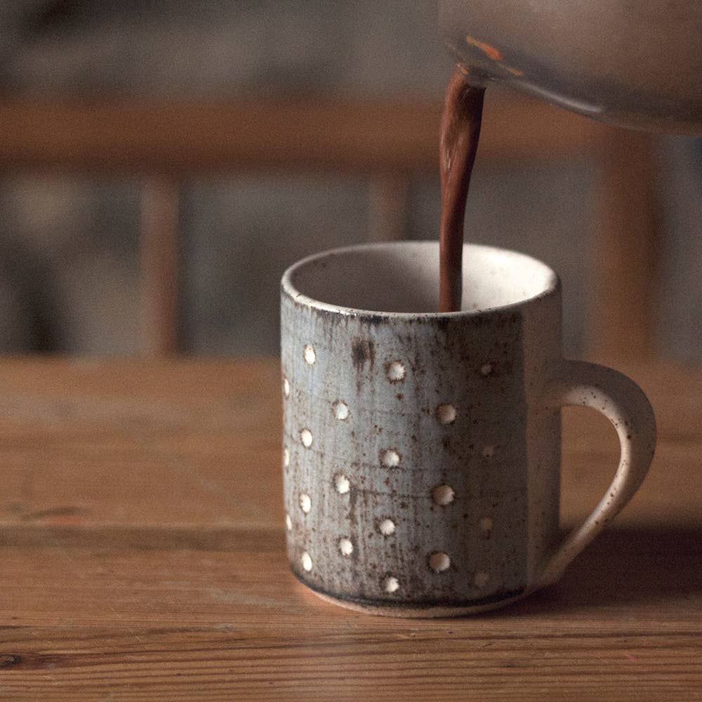 Hot chocolate being poured into a textured mug on a wooden surface.