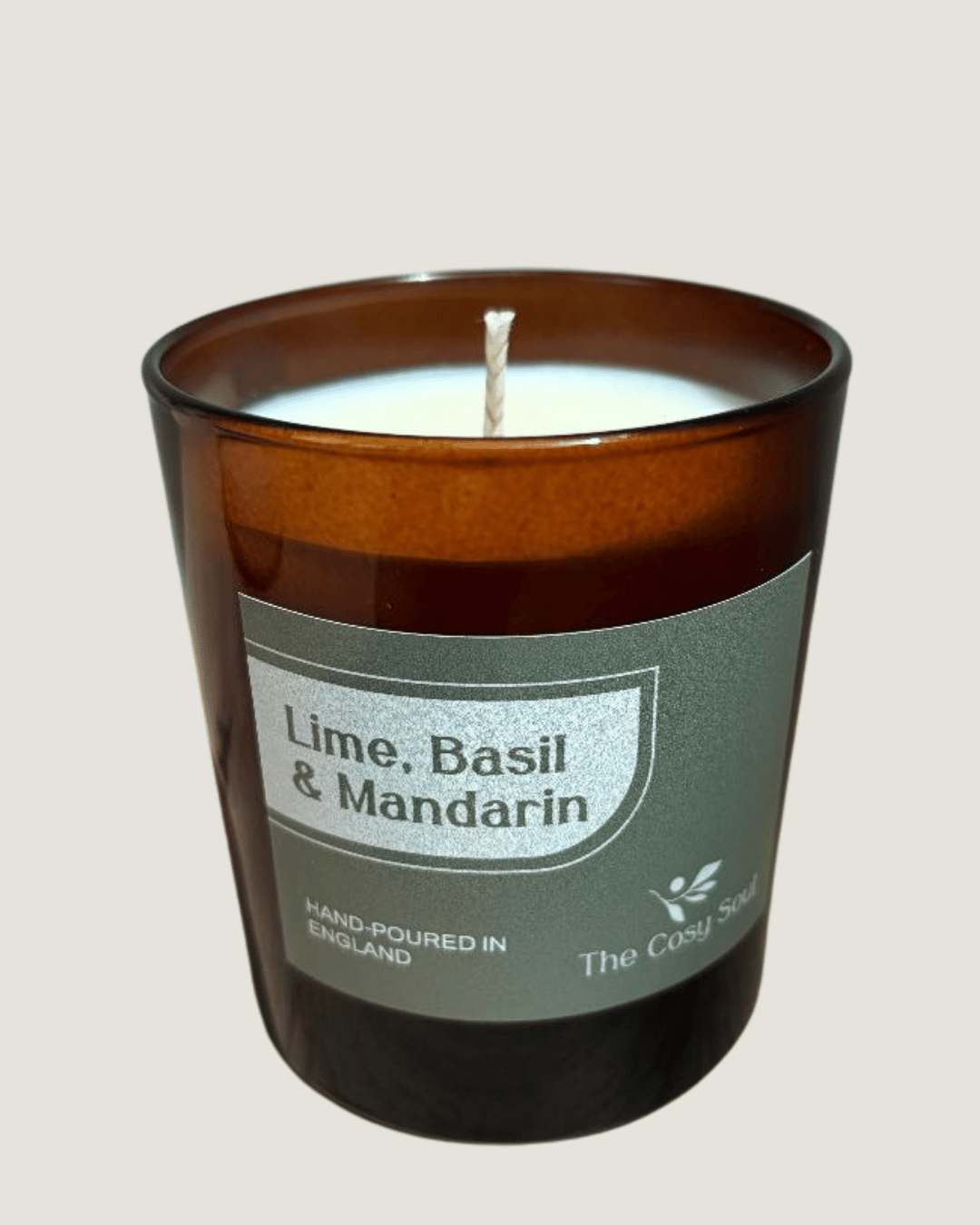 Candle with a label reading 'Lime, Basil & Mandarin' by 'The Cosy Scent' on a beige background