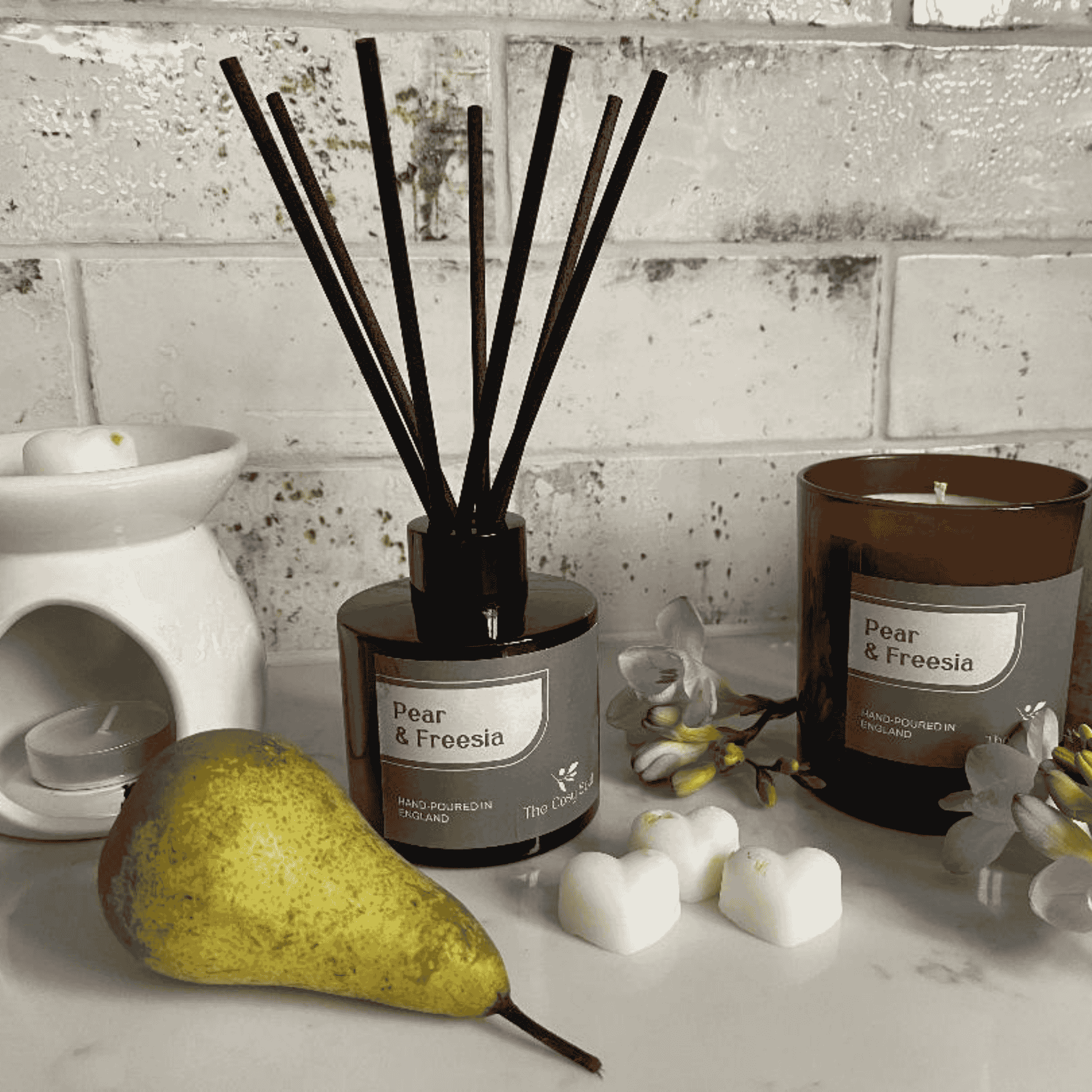 The Cosy Soul Pear and Freesia Candle, Diffuser and Wax melts  on a surface with a white brick wall background