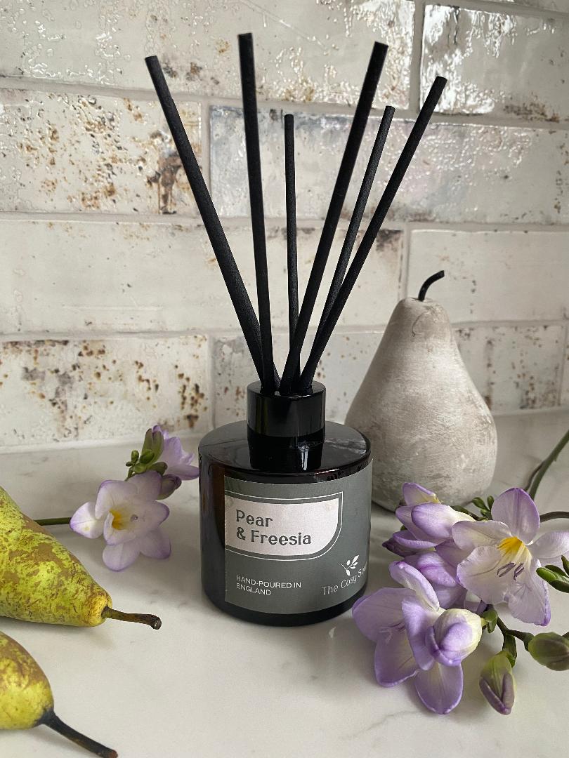 Pear and Freesia Reed Diffuser with black reeds on a white surface with pears and flowers.