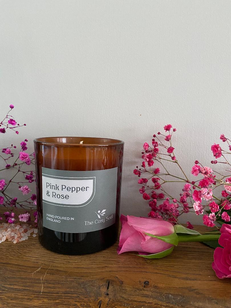 The Cosy Soul Pink Pepper & Rose candle with pink flowers on a wooden surface