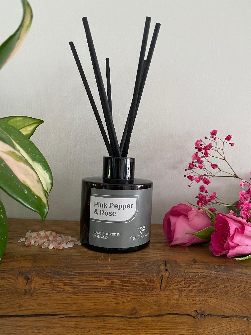 Pink Pepper and Rose Reed Diffuser with pink roses and pepper on a wooden shelf