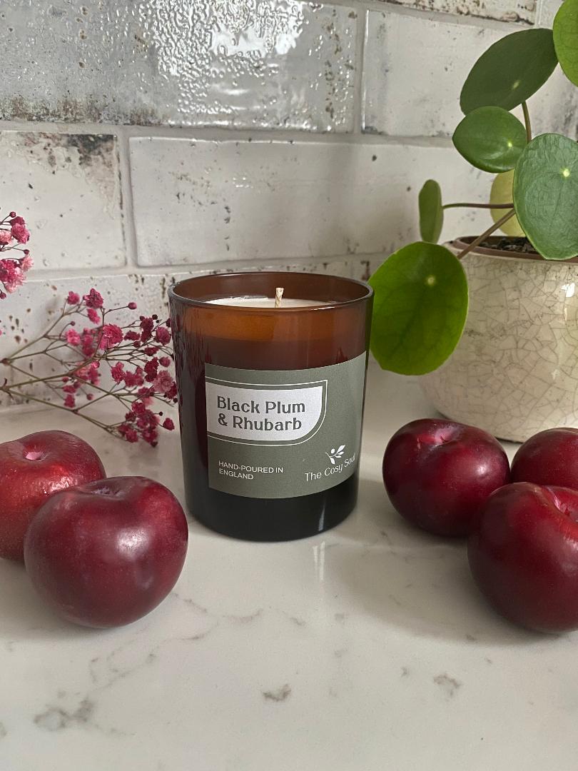 Black Plum and Rhubarb Candle in an amber jar with plums and flowers.