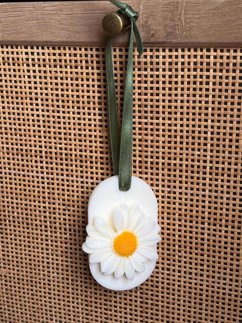 Wax melt hanging with a daisy design on a green ribbon against a woven background