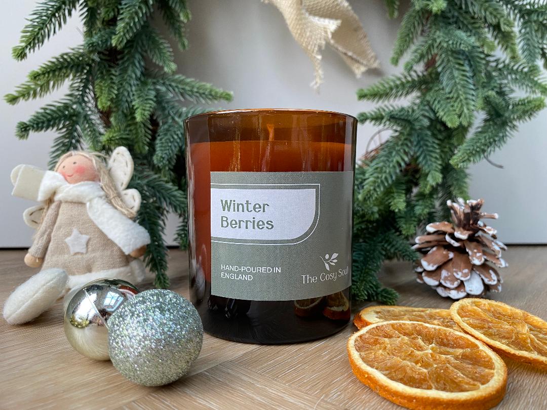 The Cosy Soul candle labelled 'Winter Berries' with Christmas decorations on a wooden surface
