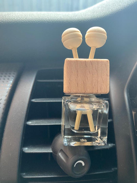 Car reed diffuser with wooden top and clear bottle in a car's vent.