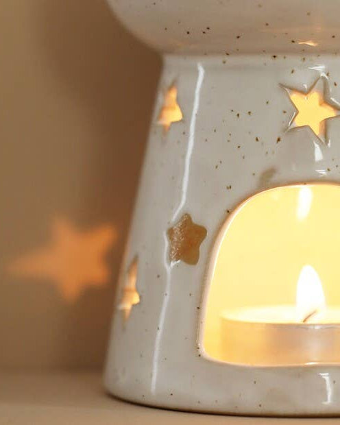 Ceramic wax melt burner with star cut-outs and a lit candle inside, casting a warm glow.