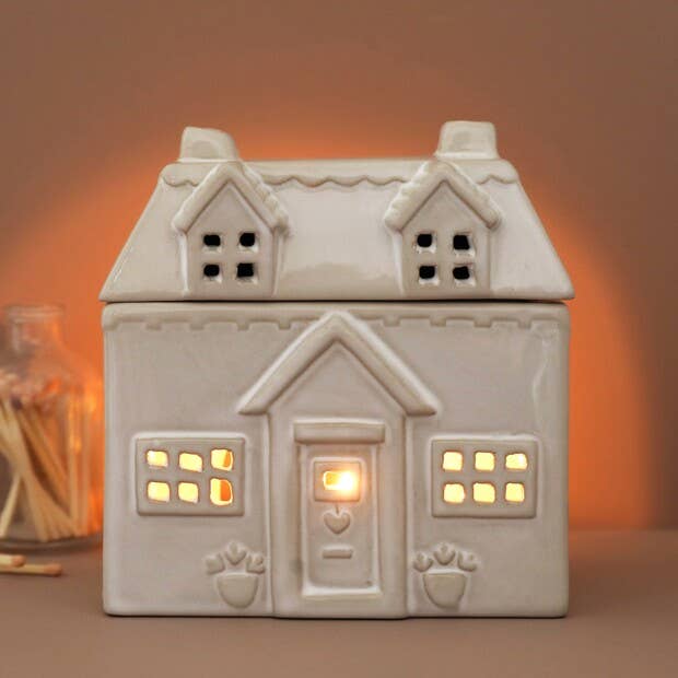 Ceramic house-shaped wax melt burner with a warm glow on a brown background