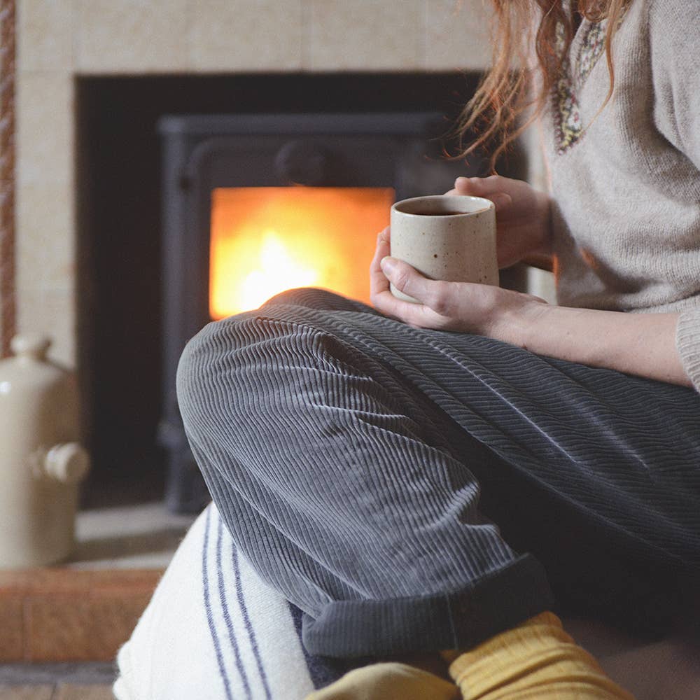Person sitting by a fireplace holding a mug of hot chocolate
