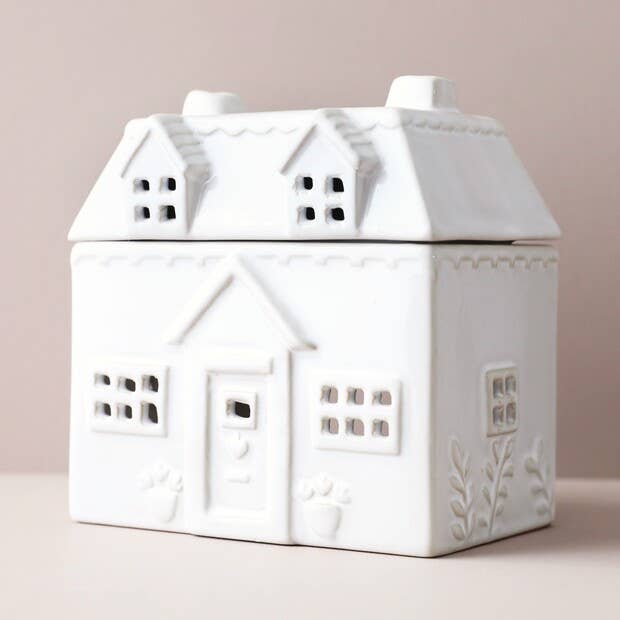 White ceramic house-shaped wax-melt burner on a light pink background