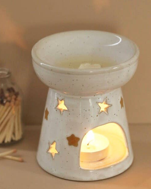 Ceramic oil burner with a lit candle inside, surrounded by matches on a beige surface.