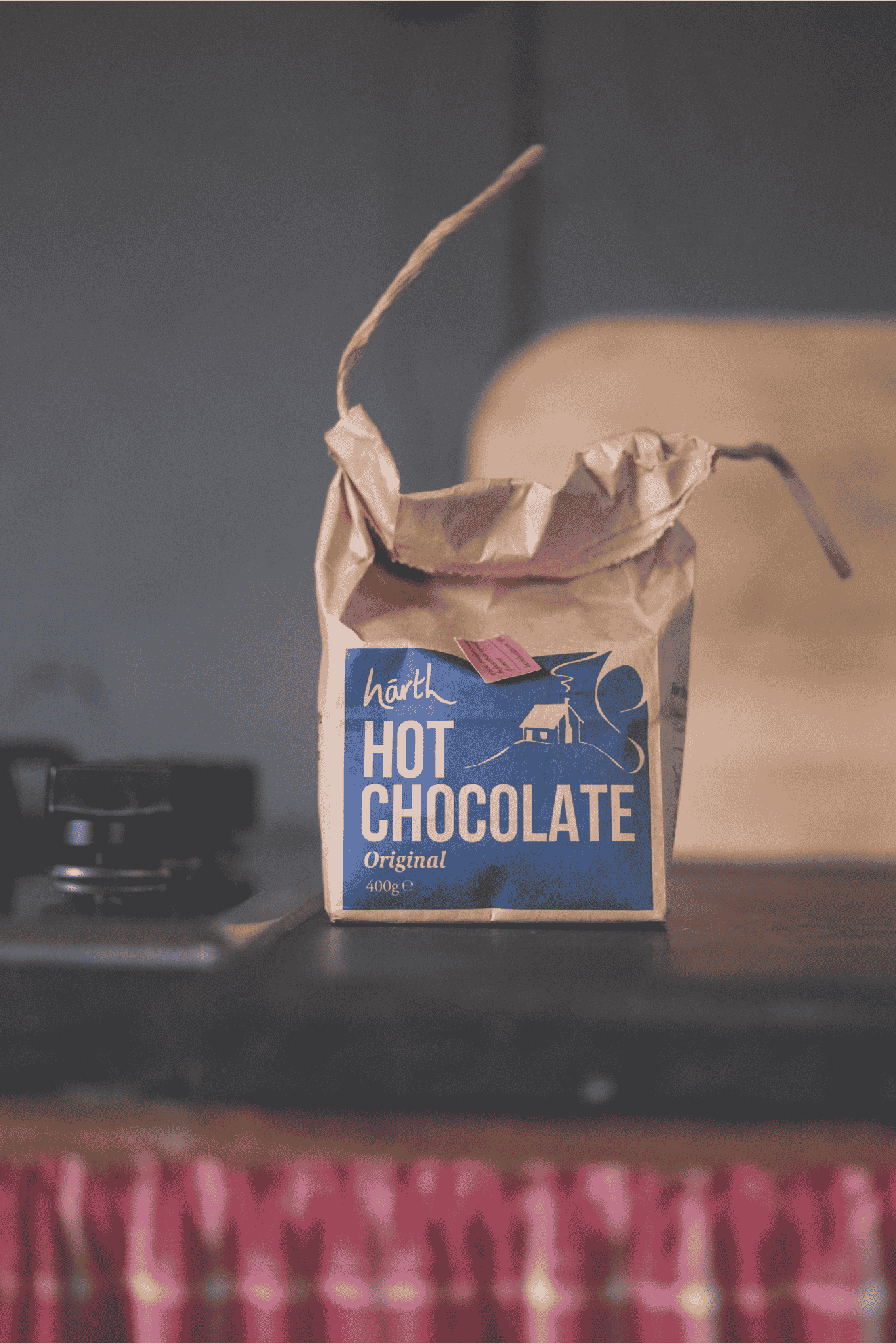 Brown paper bag of Harth Hot Chocolate on a dark surface with a blurred background