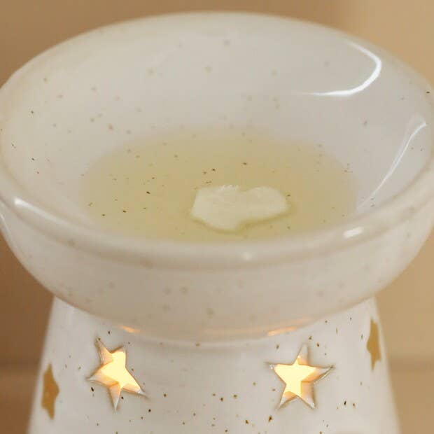 White ceramic oil burner with star designs on a beige background